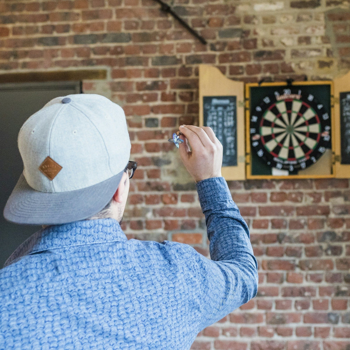 Mann zielt mit einem Dartpfeil auf eine Dartscheibe an einer Backsteinwand